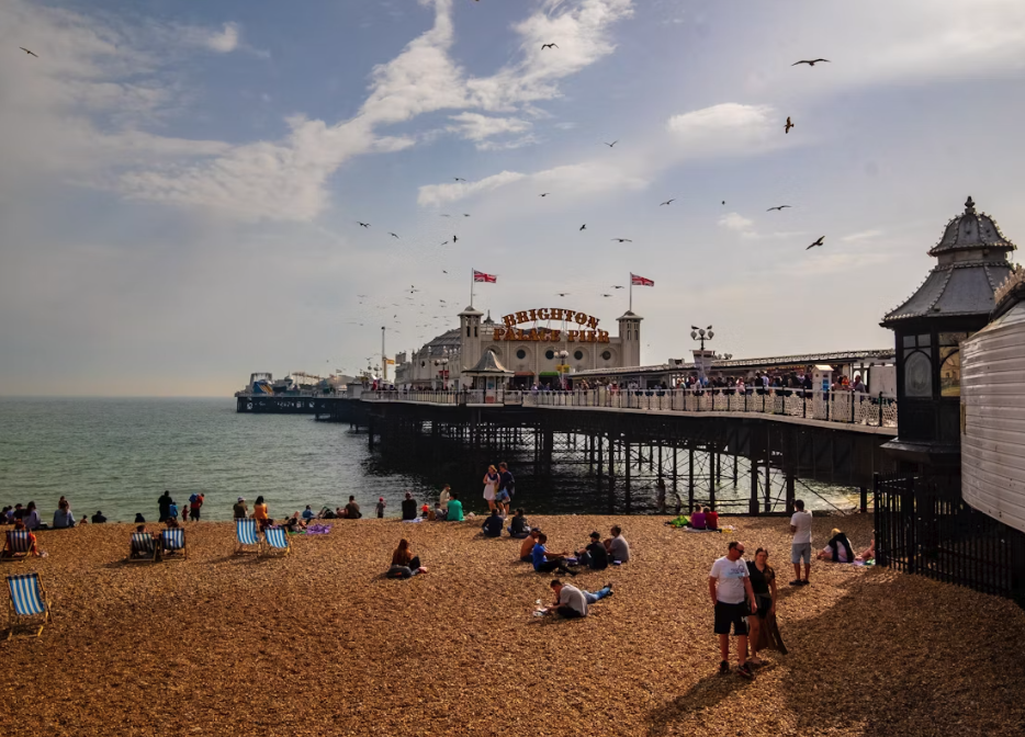 People walking next to Brighton Pier on the pebbles on a sunny day